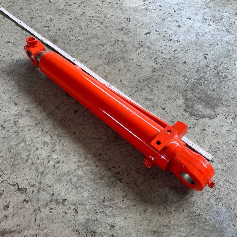 Orangefarbener Hydraulikzylinder von Kubota neben einem Zollstock auf Betonboden